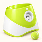Green automatic dog ball launcher with top-loading opening, white front outlet and green ball on a clean cream background