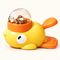 Yellow duck-shaped pet treat dispenser with orange accents and clear reservoir on a clean off-white background