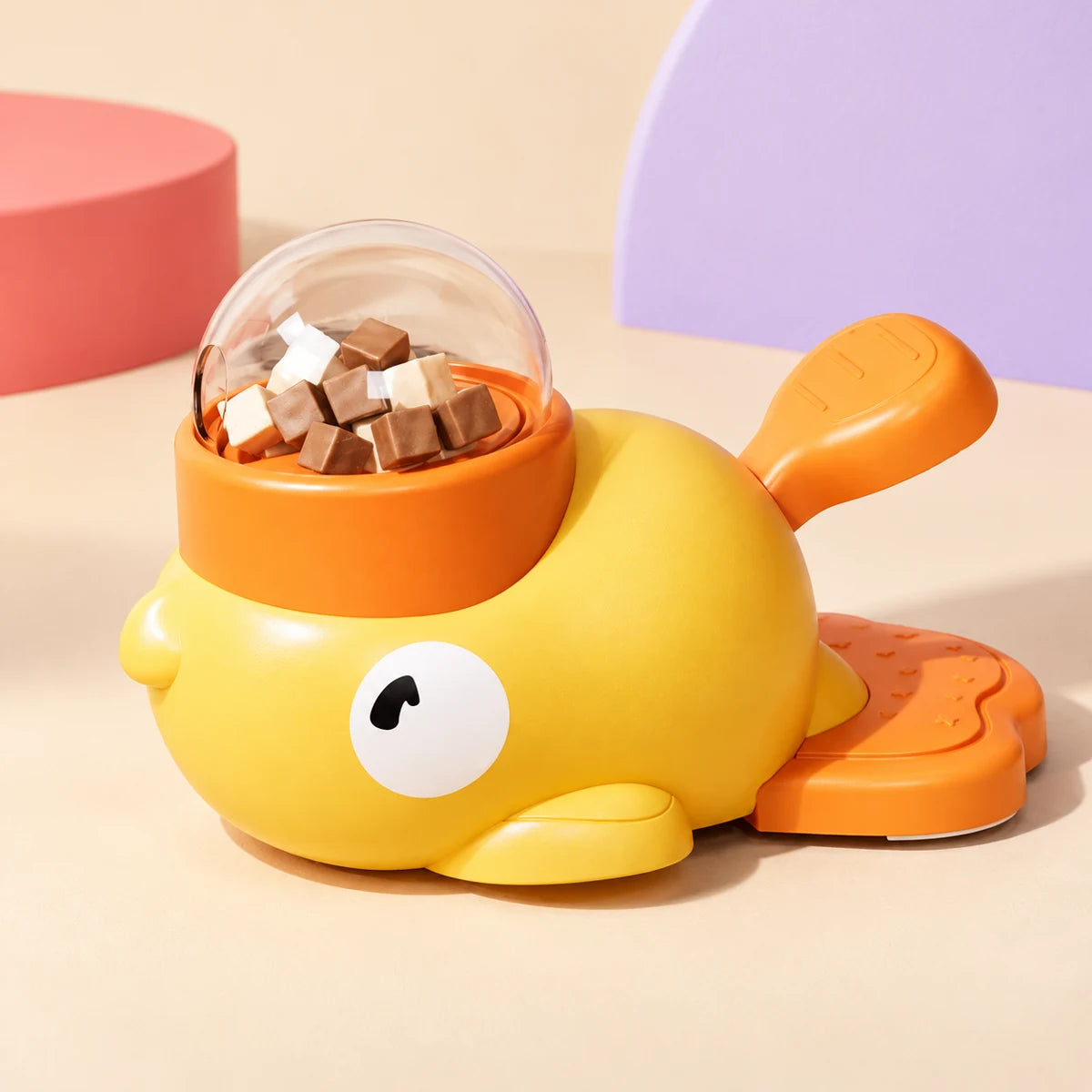 Yellow duck-shaped pet treat dispenser with orange accents and clear reservoir shown from another angle